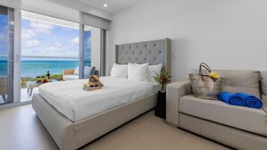 A modern bedroom with a large bed, a sofa, and a view of the ocean.