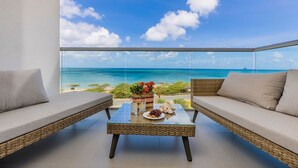 A balcony with wicker furniture, a glass table, and a view of the ocean.