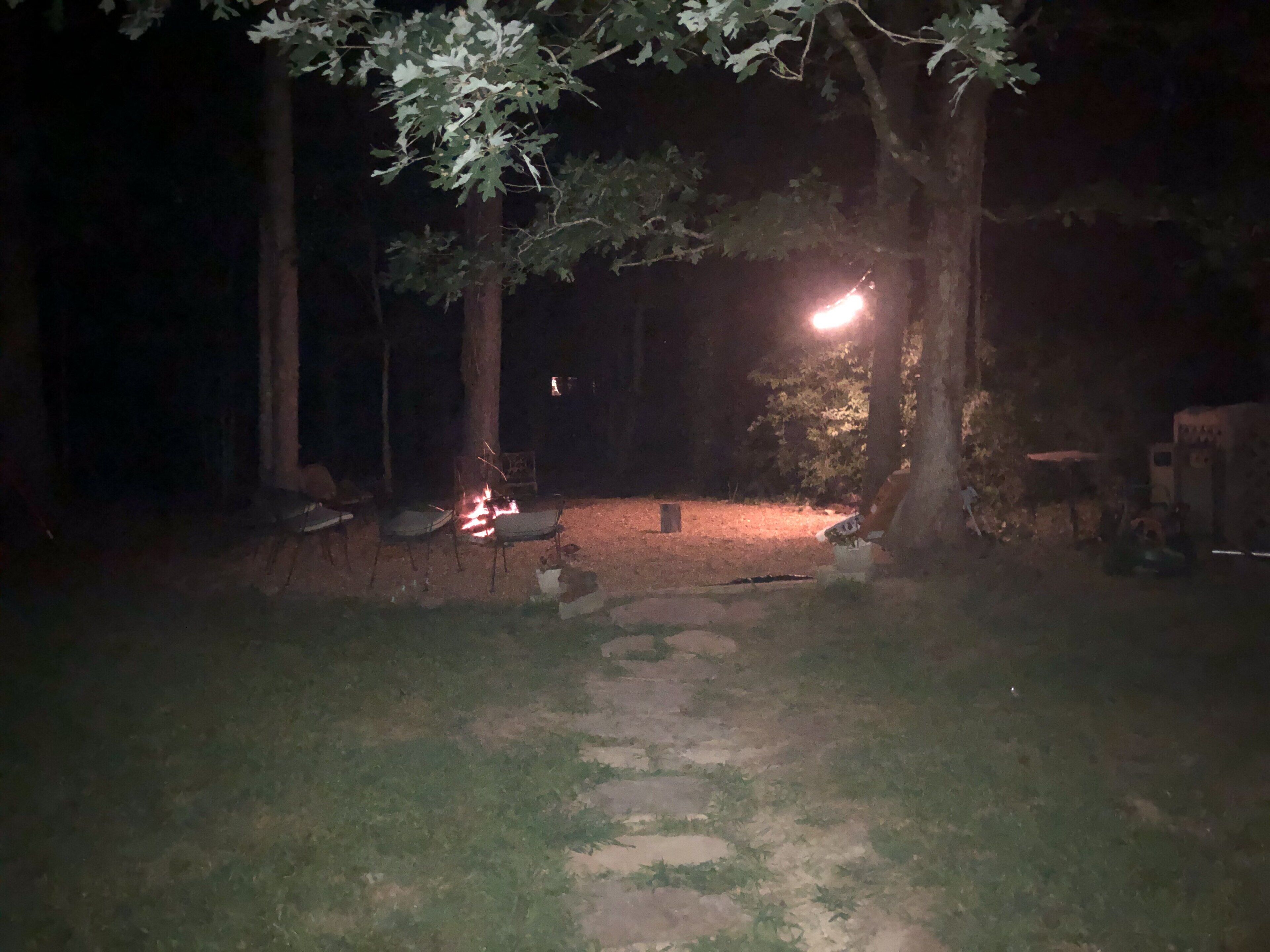 Une scène nocturne en plein air, avec un feu de camp, des arbres et un sentier pavé de pierres.