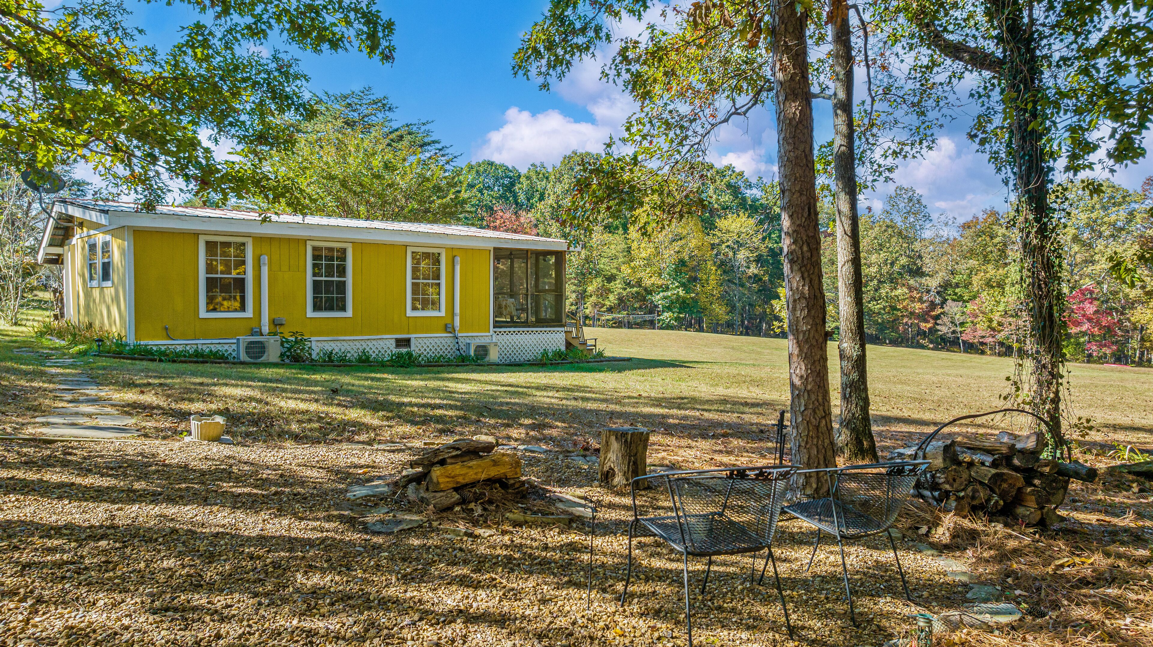 A yellow house with a porch, surrounded by trees and a grassy yard.