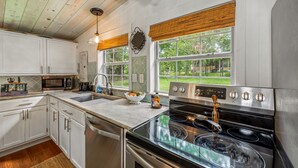 A kitchen with white cabinets, a stainless steel stove, and a large window with a view of the outdoors. - Mountain Meadow (Mentone)