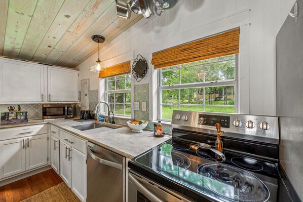 A kitchen with white cabinets, a stainless steel stove, and a large window with a view of the outdoors.