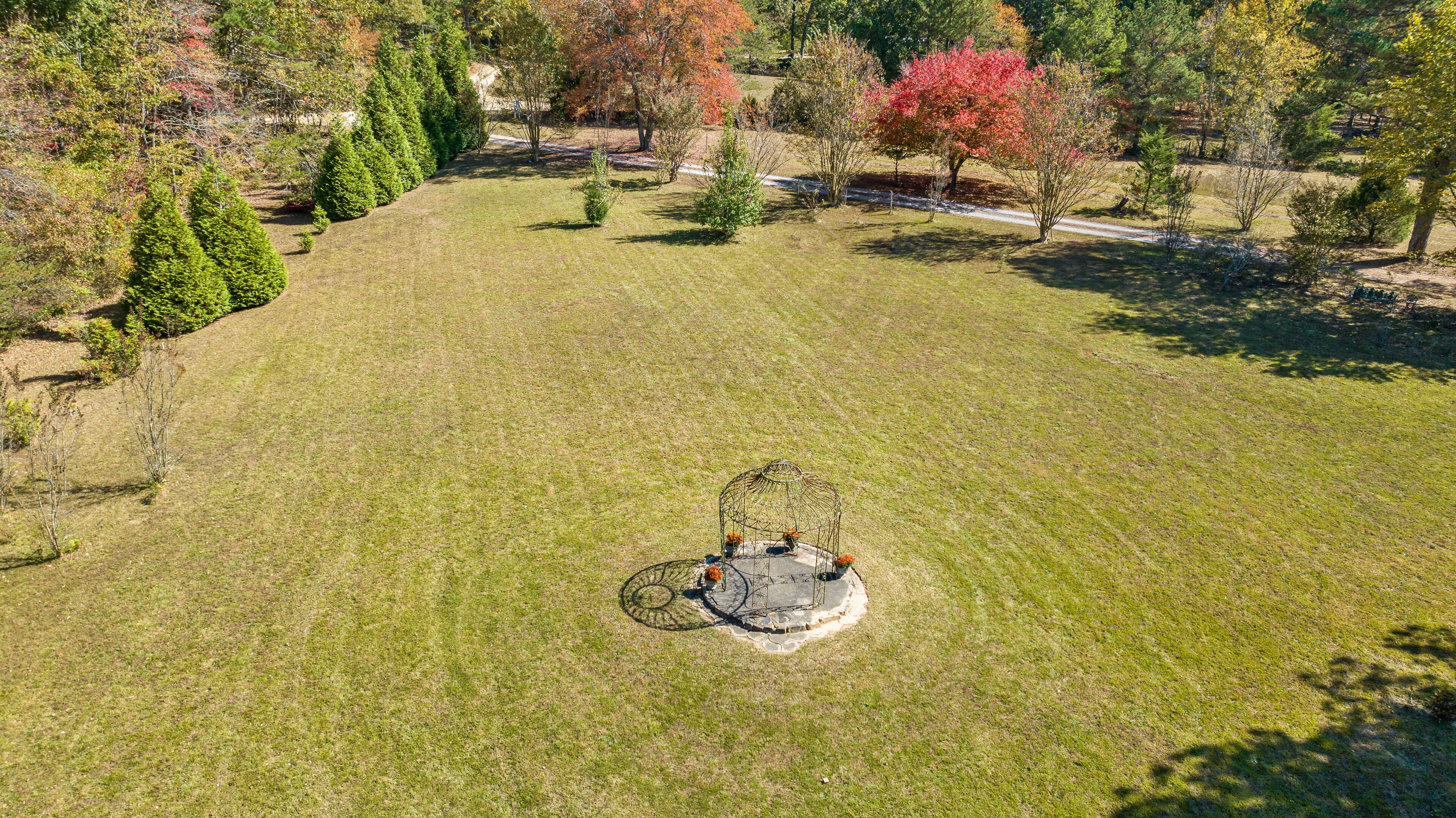 An aerial view of a large, open grassy area with a circular stone structure in the center, surrounded by trees and shrubs.