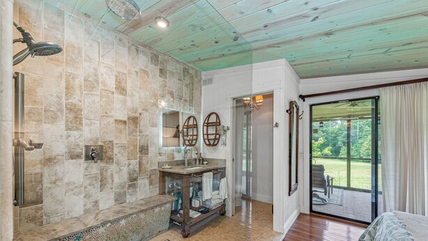 A bathroom with a stone wall, a wooden vanity, a shower, and a view of a garden through a glass door. - Mountain Meadow (Mentone)