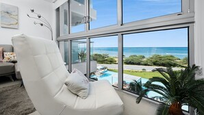 Un salon moderne doté d’une grande fenêtre donnant sur une piscine et offrant une vue sur l’océan.