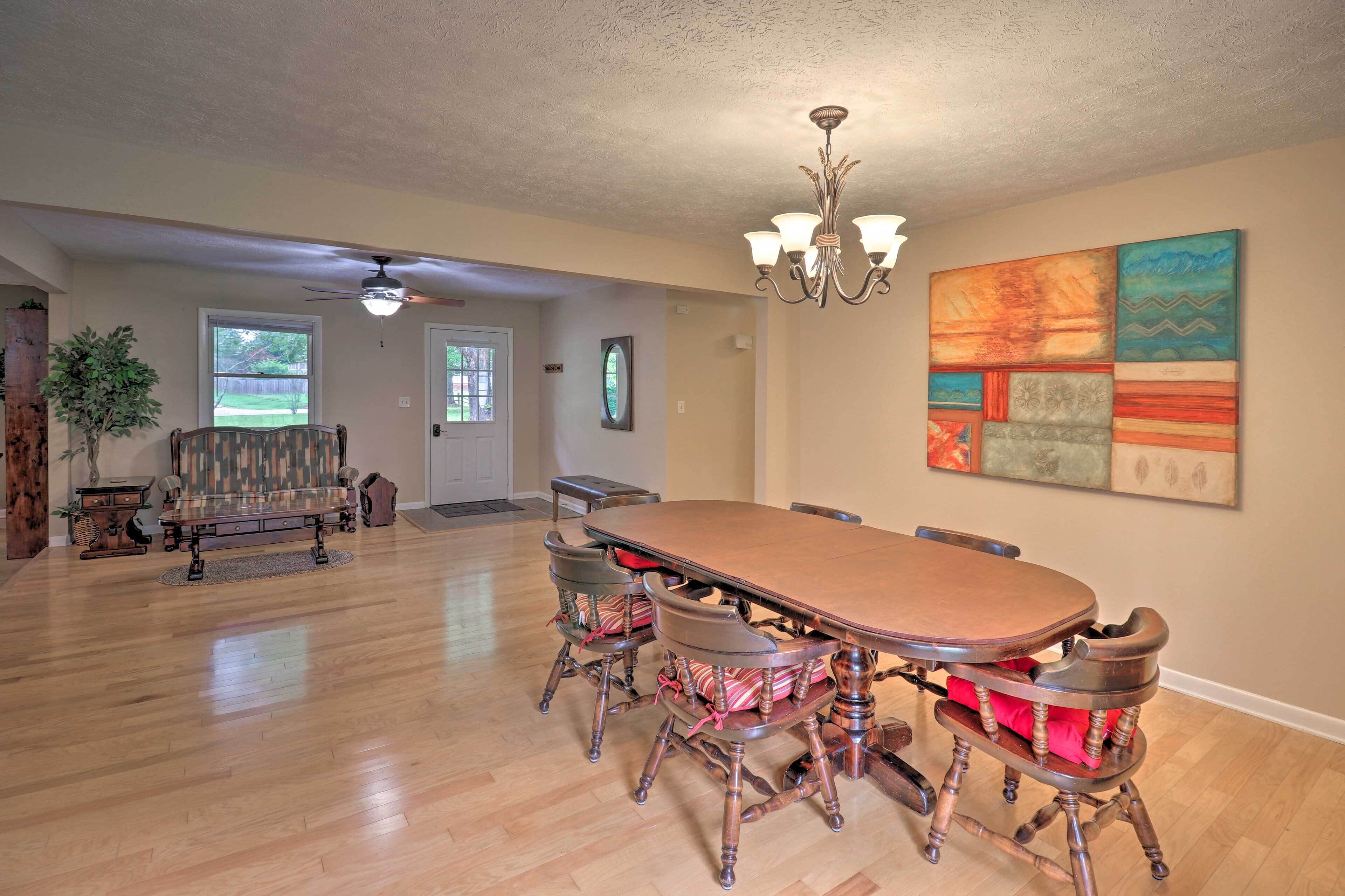 Un vaste espace dédié à la salle à manger, avec une grande table en bois et quatre chaises, un lustre et un tableau abstrait aux couleurs vives accroché au mur.