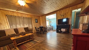 A wooden-floored living room with a sofa, coffee table, and TV. - Bunkhouse with Horse Accommodations (Big Timber)