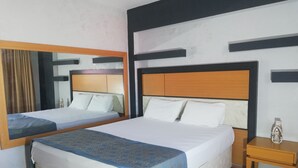 A hotel room with two beds, a wooden headboard, a nightstand, and a mirror. - Unaten Otel (Izmir)
