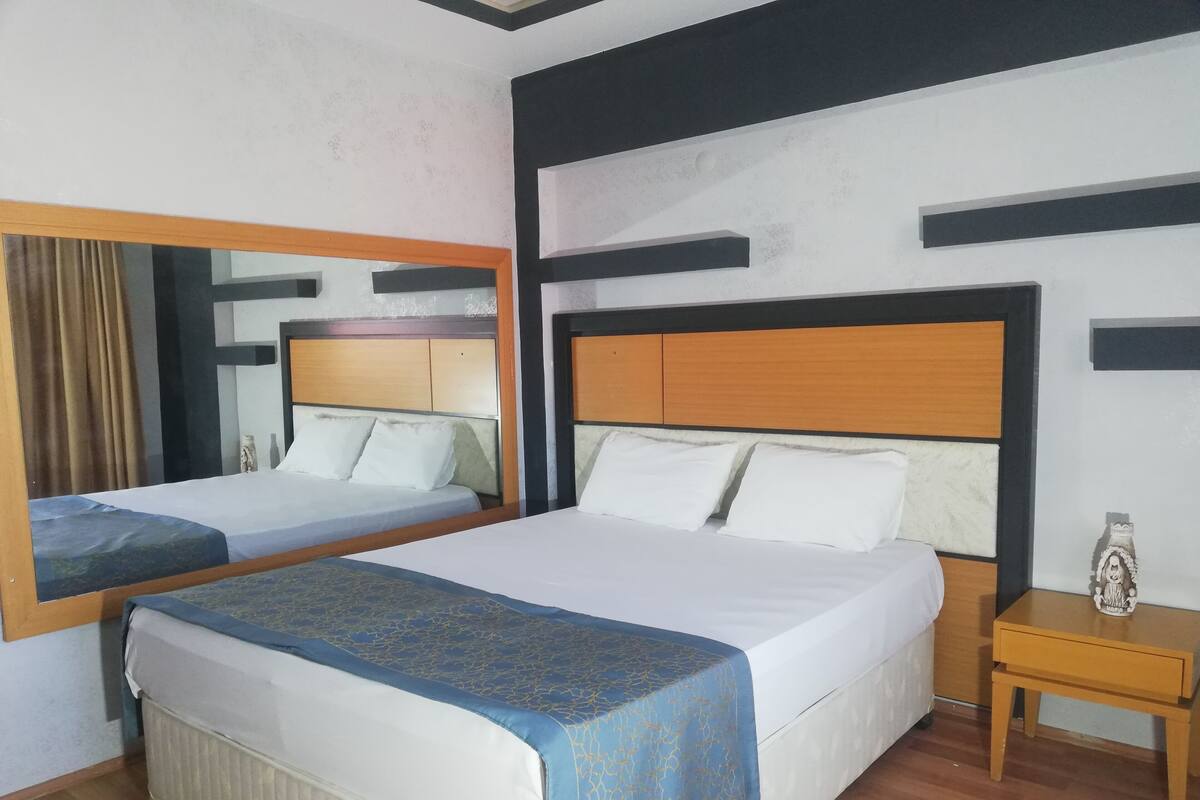 A hotel room with two beds, a wooden headboard, a nightstand, and a mirror.