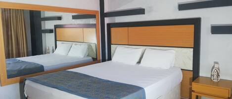 Habitación de hotel con dos camas, cabecero de madera, mesita de noche y espejo.