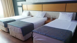 A hotel room with two single beds and a double bed, each with white linens and decorative pillows. - Unaten Otel (Izmir)