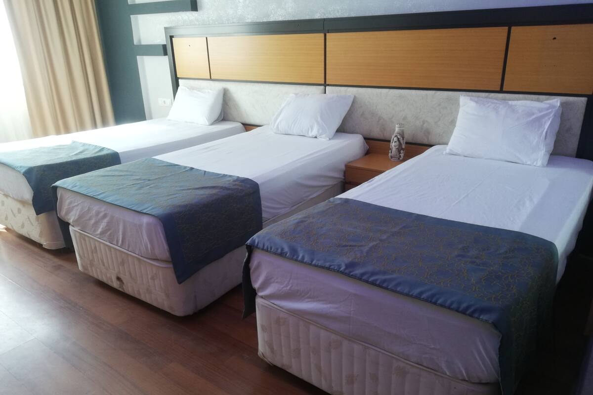 A hotel room with two single beds and a double bed, each with white linens and decorative pillows.