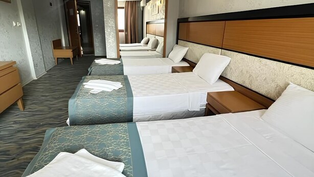 A hotel room with three beds, a chandelier, framed pictures on the wall, and a wooden headboard. - Unaten Otel (Izmir)