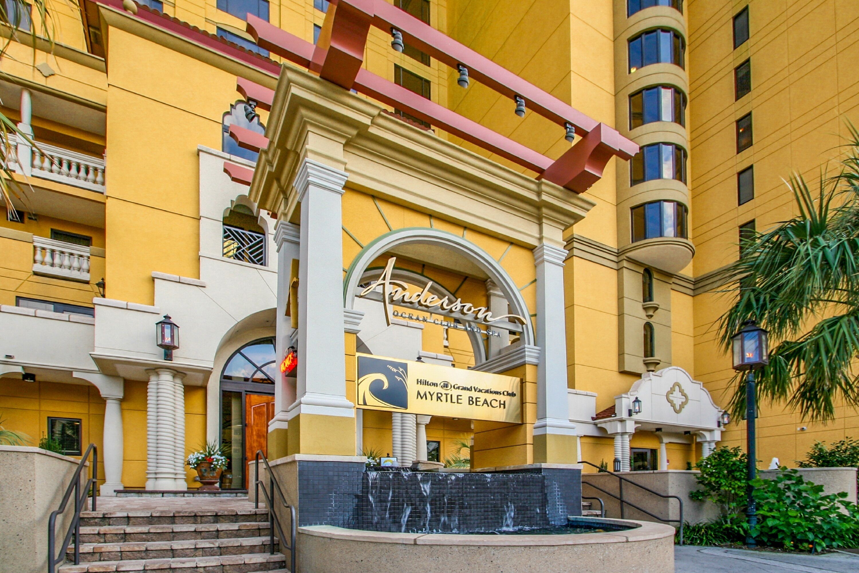 A hotel entrance with a fountain, a sign for Hilton Grand Vacations Club Myrtle Beach, and a balcony with railings.