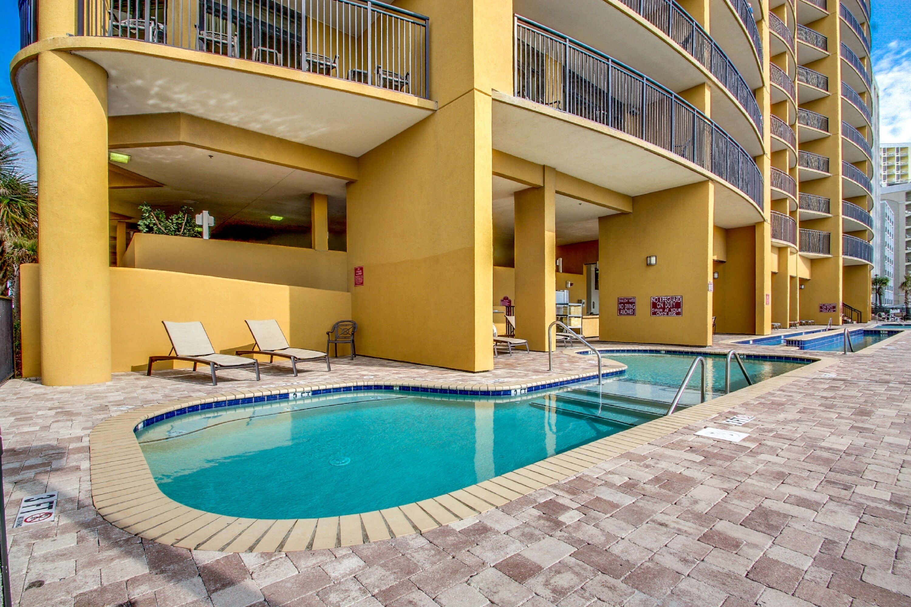 A hotel with a pool area, outdoor seating, and a yellow facade.