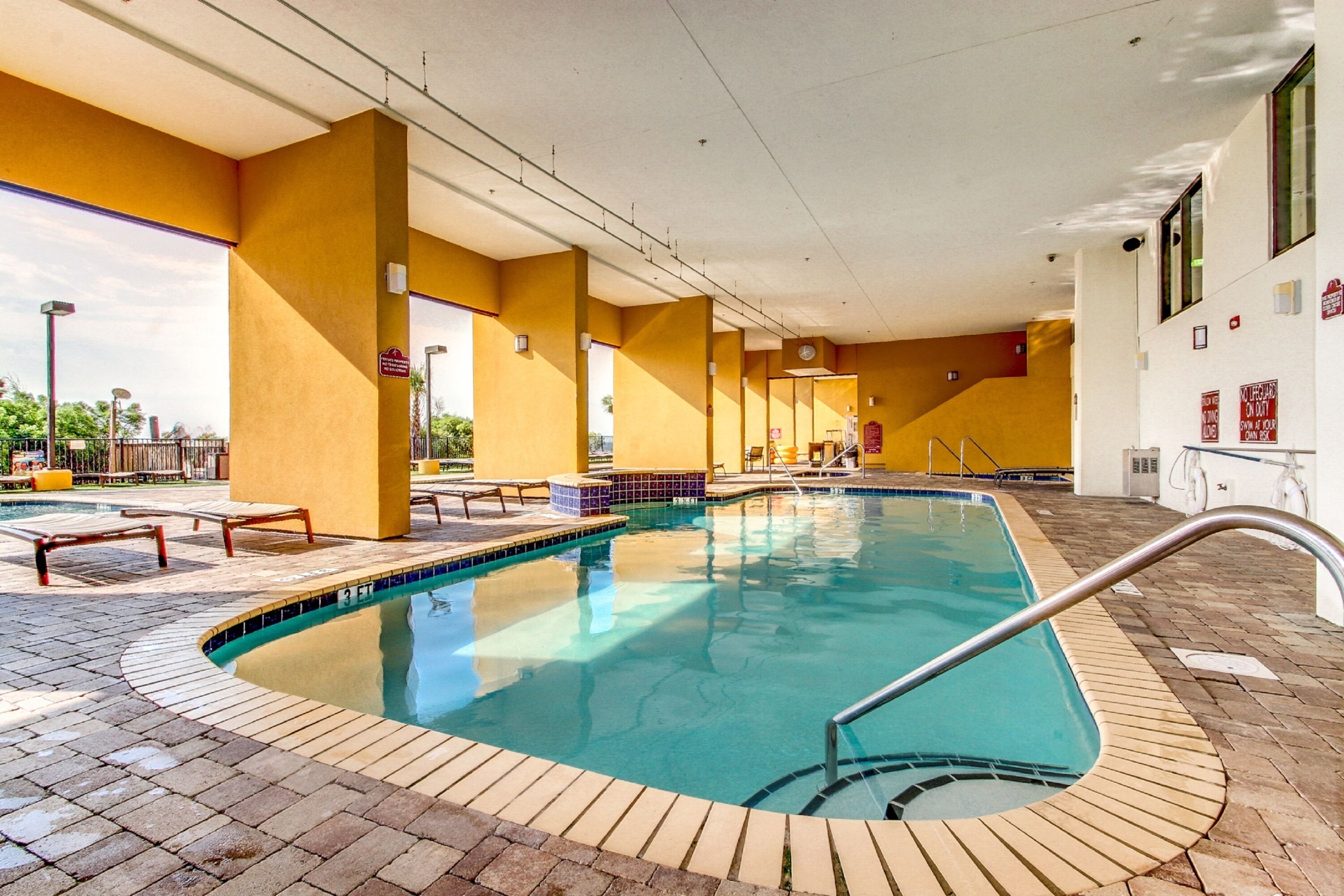 An indoor swimming pool with tiled flooring, yellow walls, and a clear blue pool.