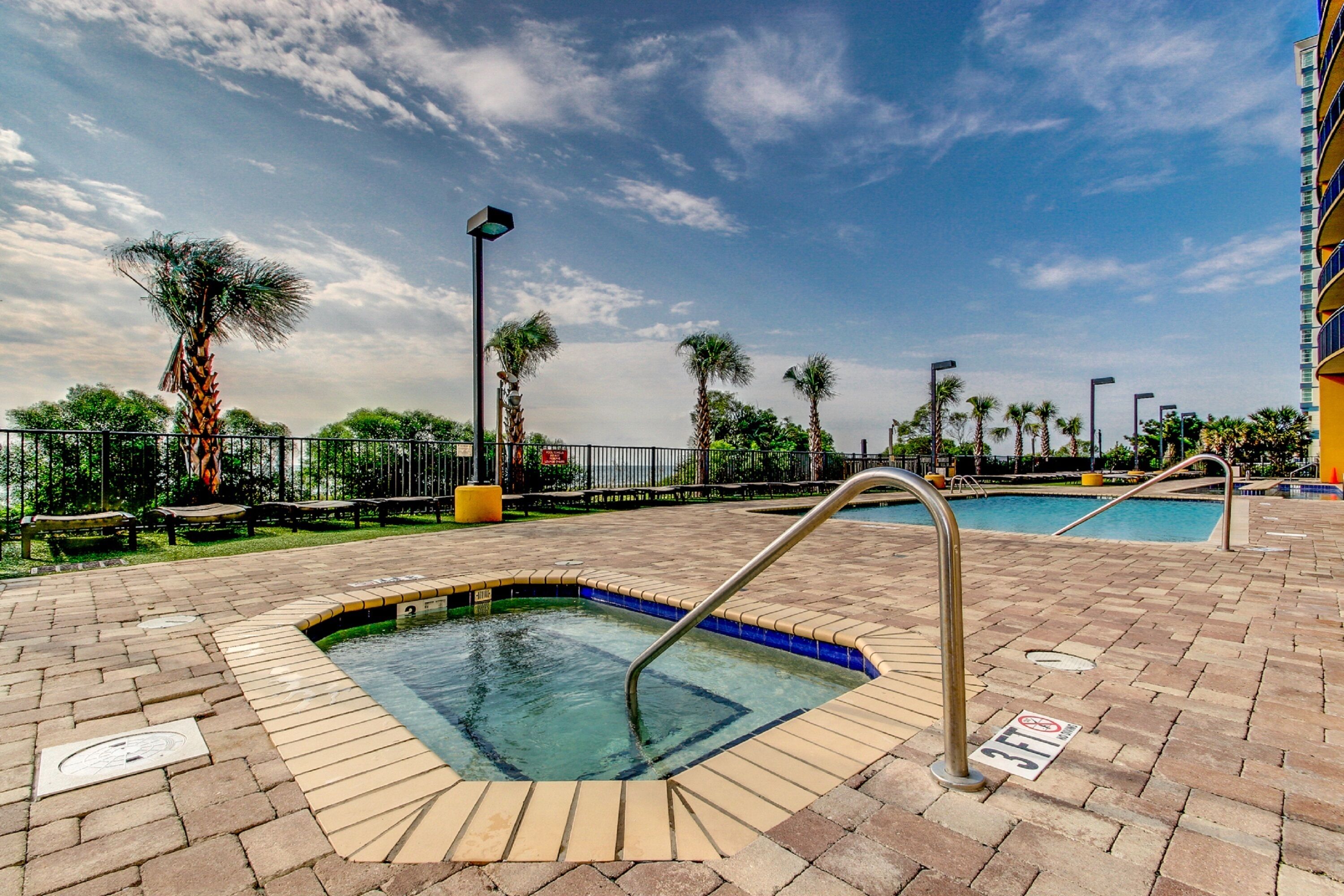 A swimming pool area with a hot tub, palm trees, and a building in the background.