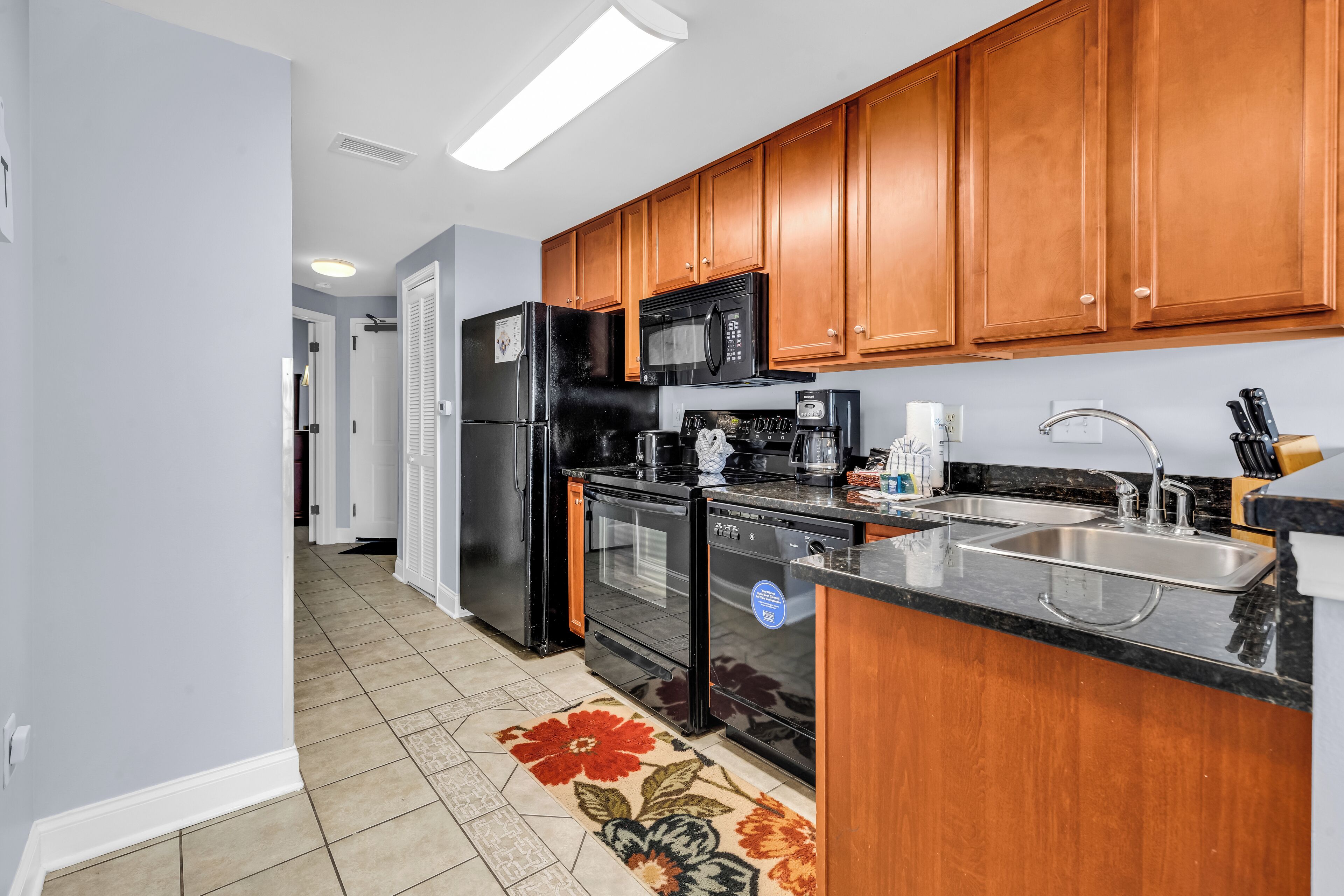 A modern kitchen with wooden cabinets, a black refrigerator, a microwave, a stove, and a sink.