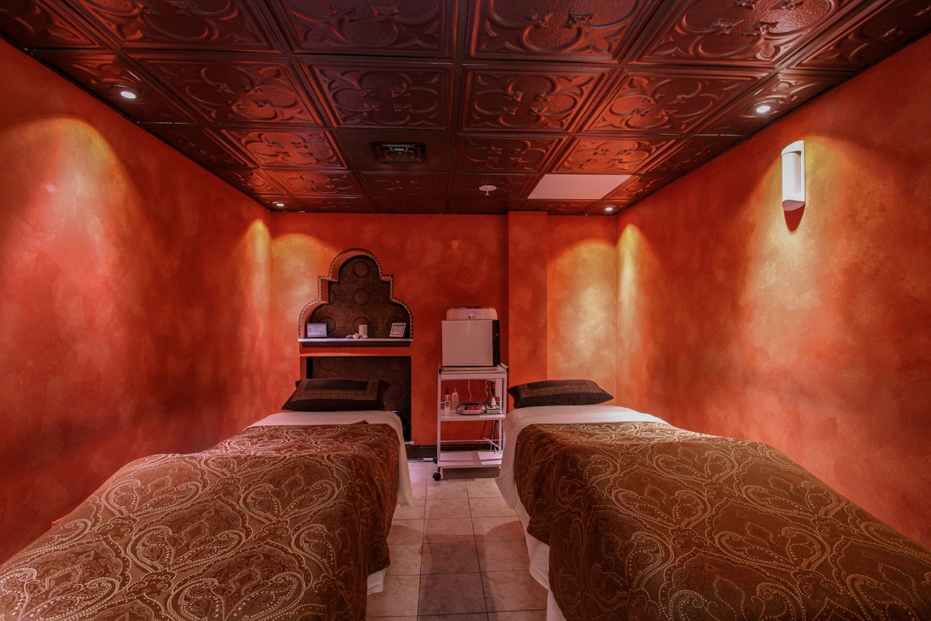 A room with two beds, a small shelf with items, and a decorative ceiling.