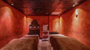 A room with two beds, a small shelf with items, and a decorative ceiling.