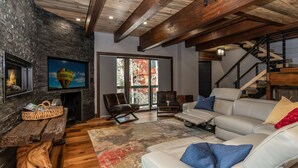 A modern living room with a stone wall, a fireplace, a large TV, leather sofas, and a staircase.