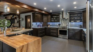 A modern kitchen with dark cabinetry, a wooden island, stainless steel appliances, and a tiled backsplash.