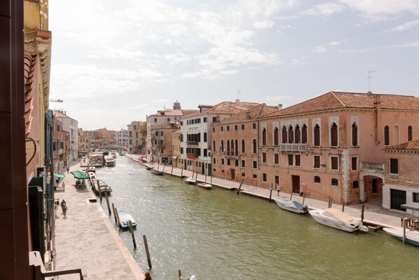 Un canal con barcos amarrados a la orilla, edificios con ventanales arqueados y un cielo despejado.
