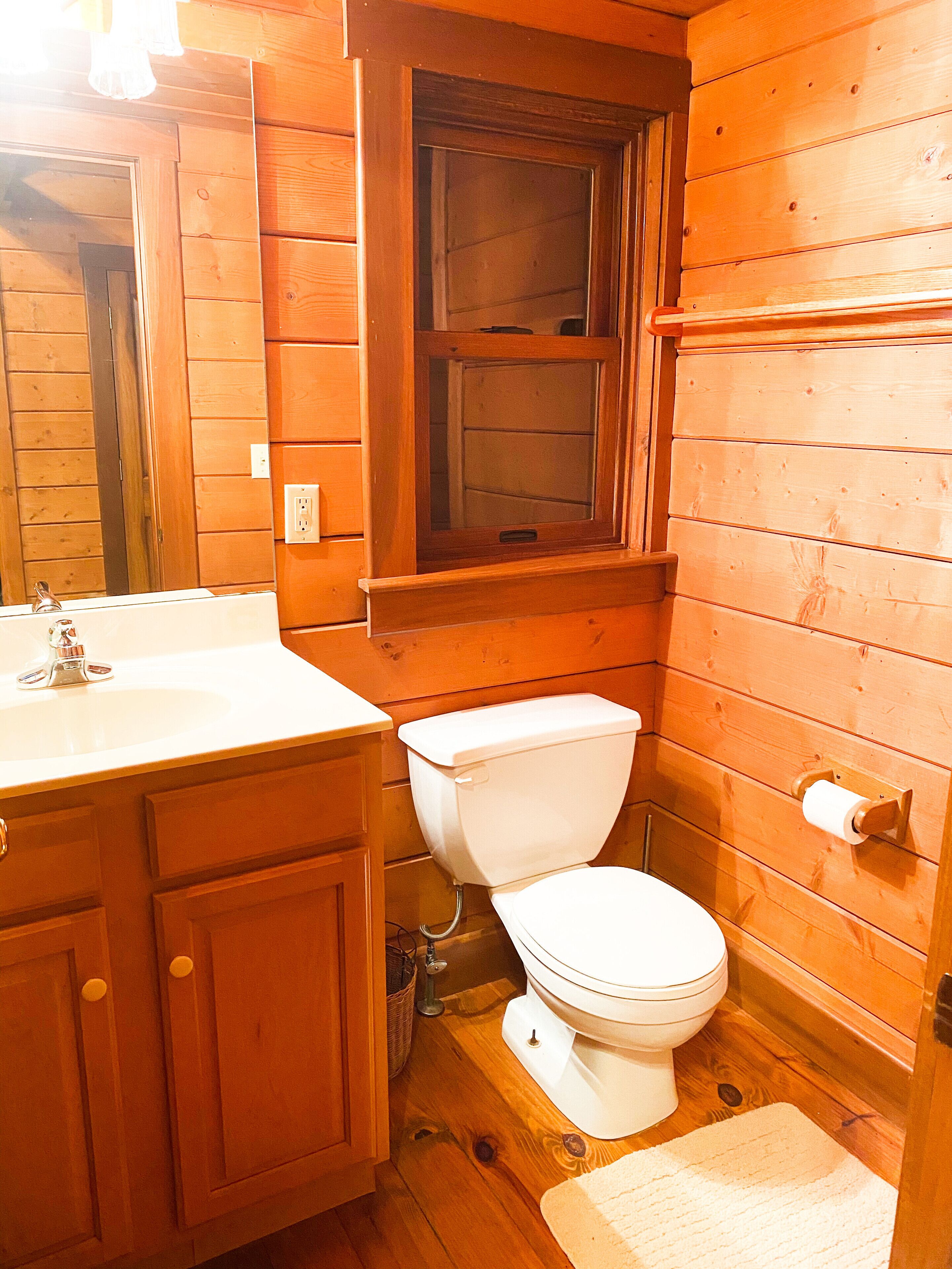 Un baño de madera con lavamanos, inodoro y ventana.