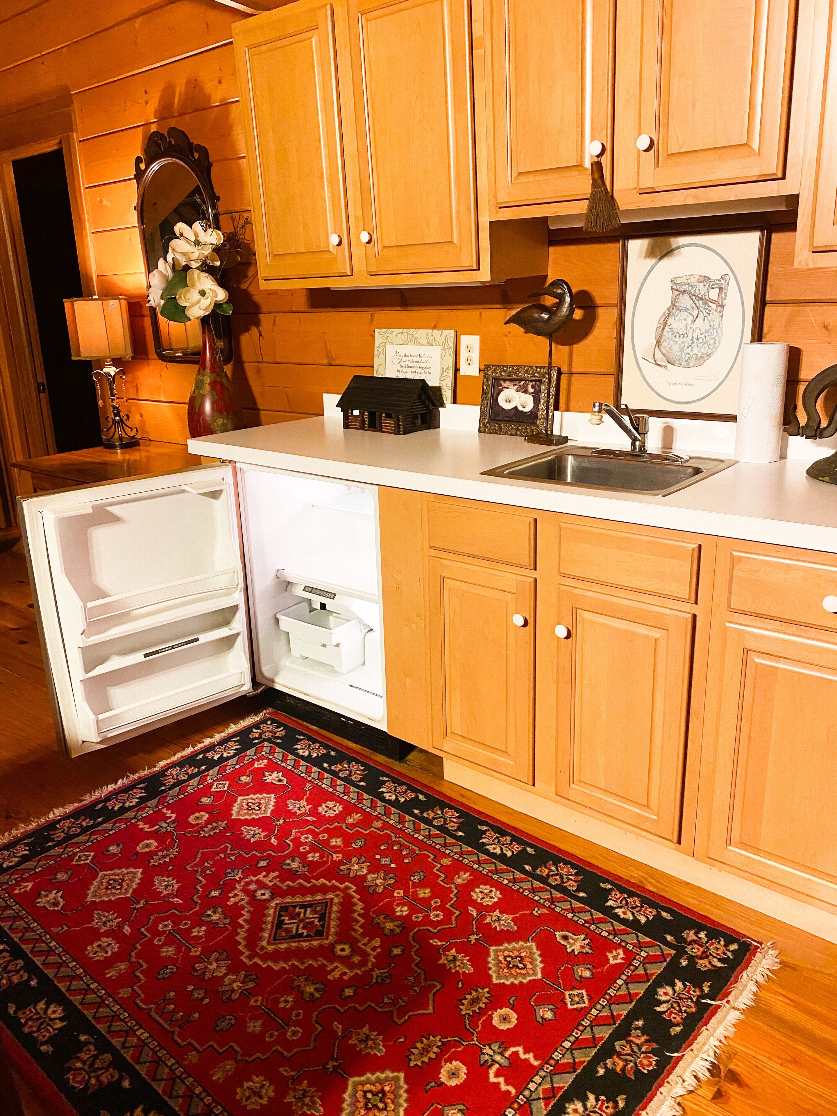 A kitchen with wooden cabinets, a sink, a refrigerator, and a decorative rug.