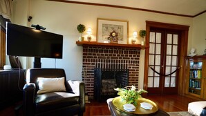 A living room with a brick fireplace, a flat-screen TV, a leather armchair, and a bookshelf. - "The In & Out Room" at TPH - Boston (Boston)