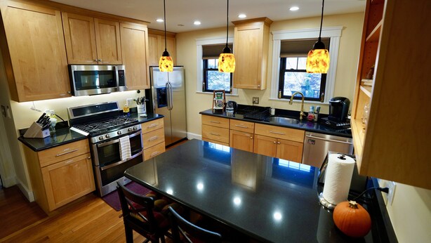 A modern kitchen with wooden cabinets, stainless steel appliances, and pendant lighting. - "The In & Out Room" at TPH - Boston (Boston)