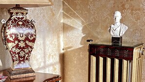 A room with a vintage lamp, a decorative vase, a bust on a wooden table, and a radiator. - "The In & Out Room" at TPH - Boston (Boston)