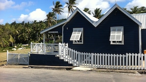 Une maison bleu foncé avec une clôture blanche en bois, un porche abrité et une enseigne sur laquelle on peut lire « Dennis Monie ».