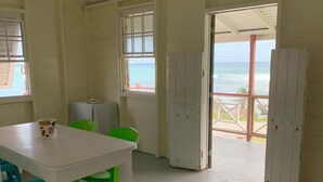 Une pièce avec une table et des chaises blanches, une fenêtre donnant sur l’océan et une porte menant à l’extérieur.