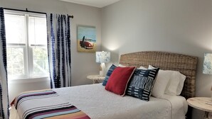 A bedroom with a large bed, a bedside table, a lamp, and a window with curtains. - Island House D : Stylish Updated Townhome - Steps to the Beach w/ Pool! (Surfside Beach)