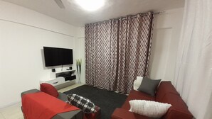 Ein Wohnzimmer mit einem Flachbildfernseher, zwei Sofas, einem Couchtisch und einem gemusterten Vorhang.