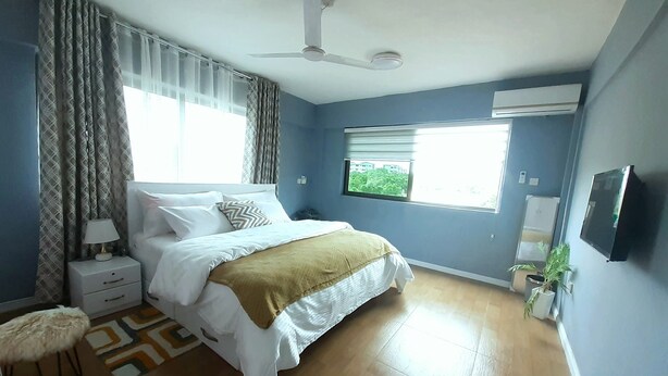 Ein Schlafzimmer mit Bett, Nachttisch, Lampe, Fenster und Deckenventilator.