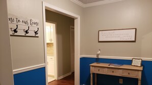 Un couloir avec un plancher en bois, un mur bleu et blanc, une porte blanche et une petite table sur laquelle est posé un panneau.