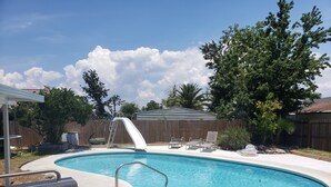 Un jardin avec une piscine, un toboggan et un espace patio couvert.