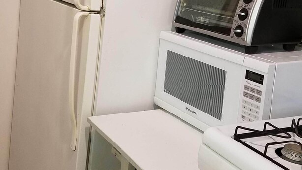 Eine kompakte Küche mit einem weißen Kühlschrank, einer Mikrowelle, einem Gasherd und einem kleinen Tisch.