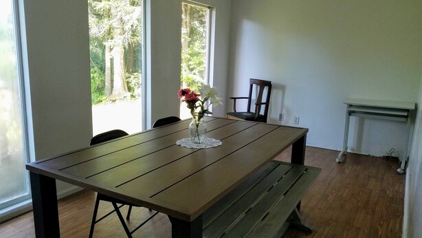 Un comedor con una mesa de madera, un banco y sillas. Hay un florero con flores sobre la mesa.