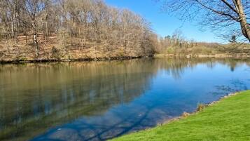 A calm river with grassy banks and leafless trees under a clear blue sky.