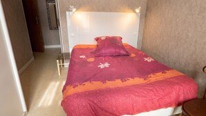 A bedroom with a bed, a bedside table, a chair, a mirror, and a door.