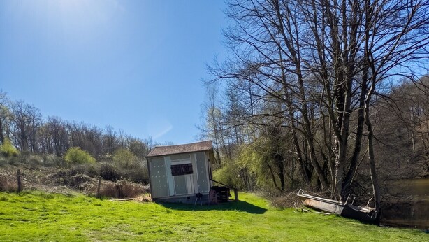 A grassy field with a small building and leafless trees.