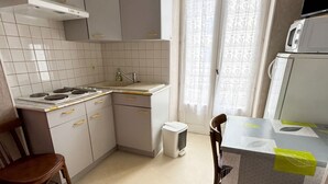 A compact kitchen with a stove, sink, and microwave. There's a dining table with chairs and a bed with a pink blanket.