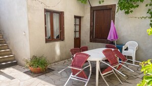 A patio with a round table and red chairs, a potted plant, and a purple umbrella.