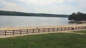 Une vue sur le lac, avec une clôture en bois, des zones herbeuses et une plage de sable.