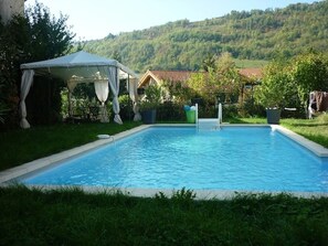 Ein rechteckiger Swimmingpool mit weißem Sonnensegel und einem Haus im Hintergrund.
