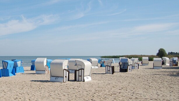 Strandhutten genummerd 34, 13, 15, 04 en 07 op een zandstrand, met de zee op de achtergrond.