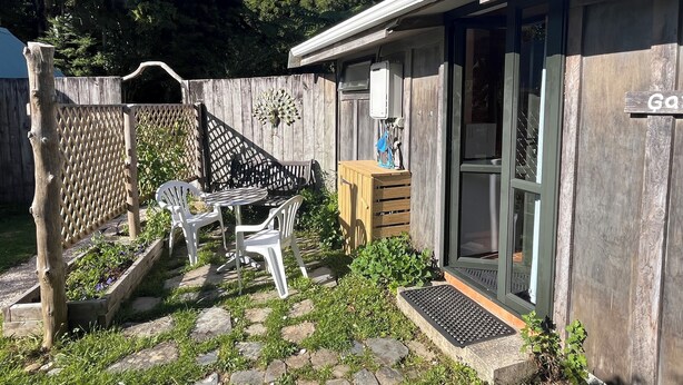 A small house with a wooden deck, a patio table and chairs, and a wooden fence. - The Garden Flat: a country apartment close to the beach and daywalks. (Collingwood)